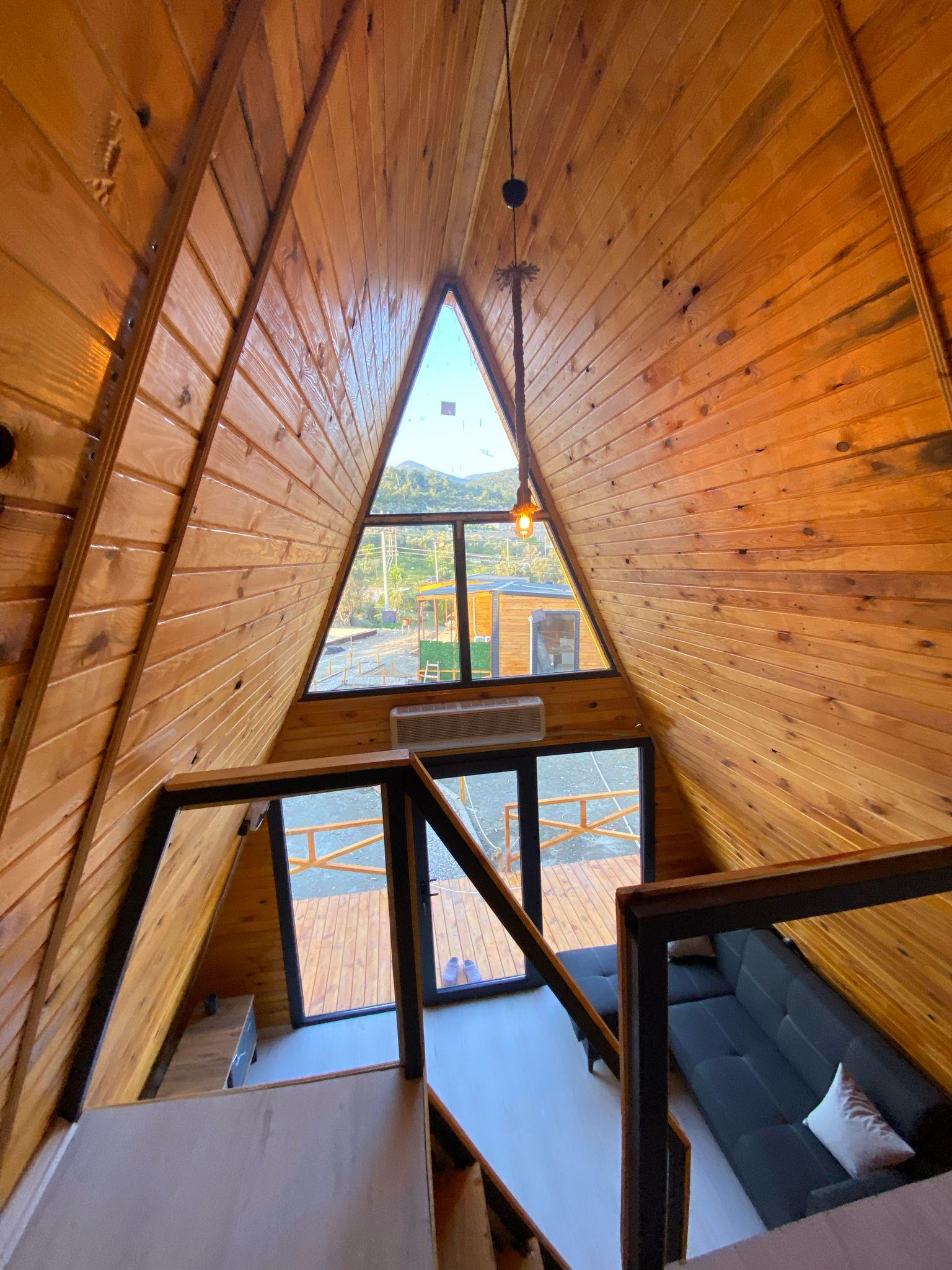 Orman içinde ahşap bungalov, sabah güneşi ağaçların arasından süzülüyor, doğal toprak ve yeşil tonlar hakim